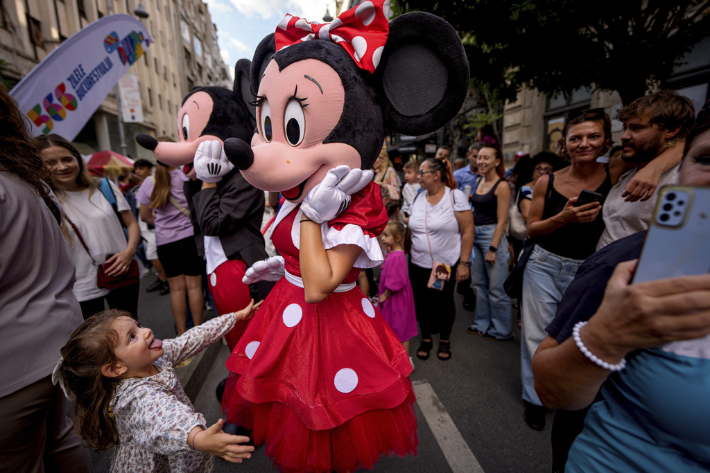A child tries to hug an entertainer wearing a Minnie Mouse costume during a parade marking the day when the Romanian capital was first mentioned in historical records, 566 years ago, in Bucharest, Romania, Saturday, Sept. 20, 2025. (AP Photo/Andreea Alexandru)