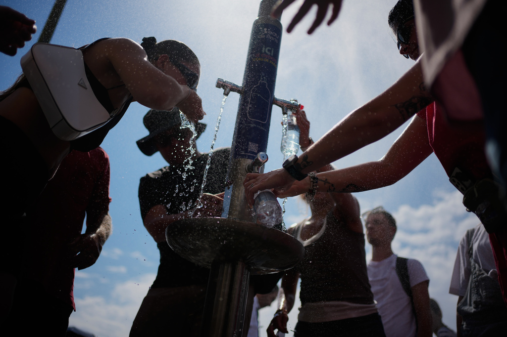 Tourists cool off at a public water fountain In Paris, Friday, June 26, 2026. (AP Photo/Christophe Ena )