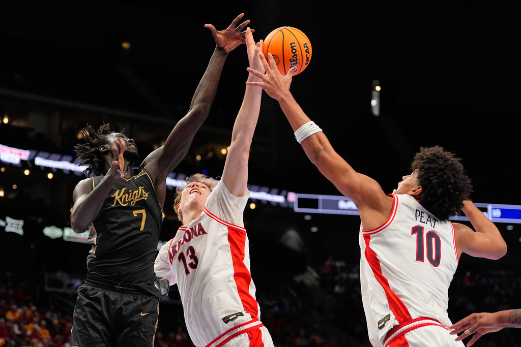 UCF's John Bol (7) reaches for a rebound along with Arizona's Motiejus Krivas (13) and Koa Peat (10) during the first half of an NCAA college basketball game in the quarterfinal round of the Big 12 Conference tournament Thursday, March 12, 2026, in Kansas City, Mo. (AP Photo/Charlie Riedel)