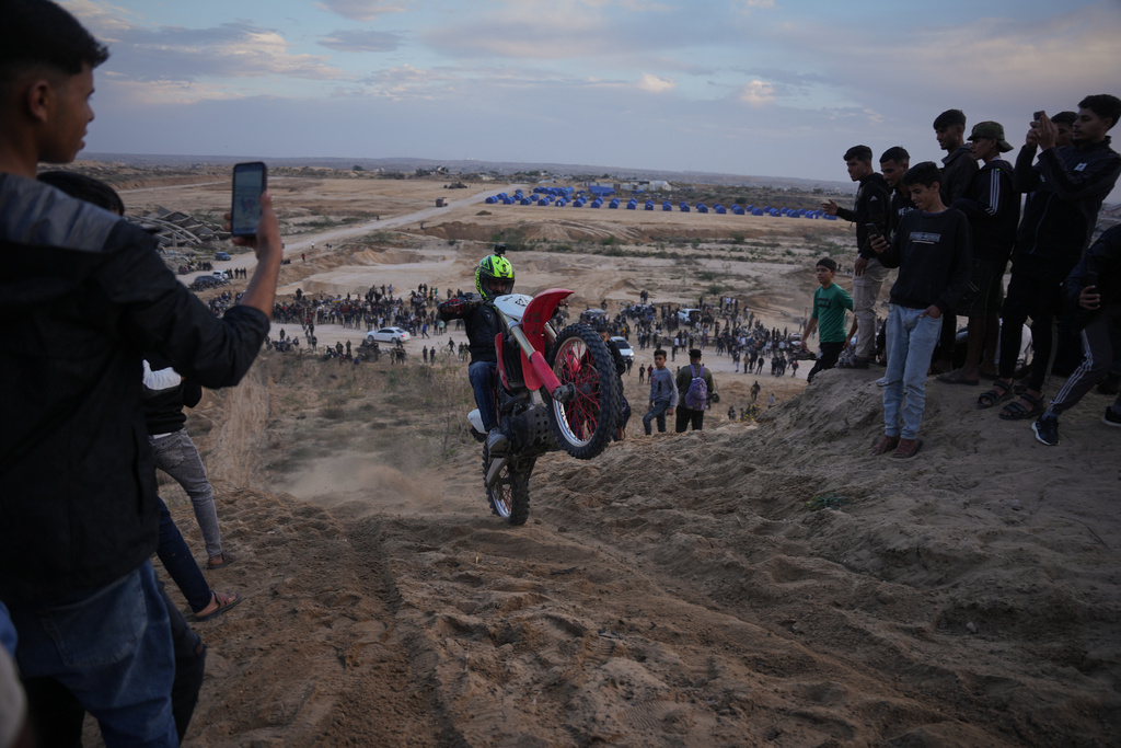 Palestinians watch youths riding their motorcycles on sand dunes in the Al-Zahra area, in the central Gaza Strip, Friday, Dec. 5, 2025. (AP Photo/Abdel Kareem Hana)