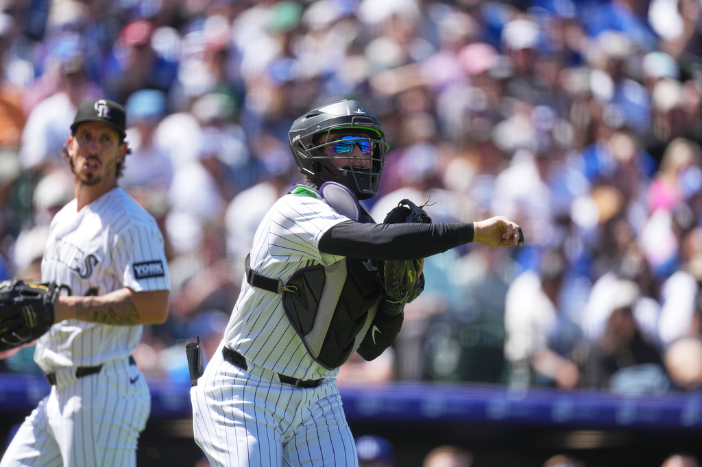 Colorado Rockies starting pitcher Michael Lorenzen, left, looks on as catcher Hunter Goodman, right, throws to first base to put out Los Angeles Dodgers' Kyle Tucker in the third inning of a baseball game Sunday, April 19, 2026, in Denver. (AP Photo/David Zalubowski)