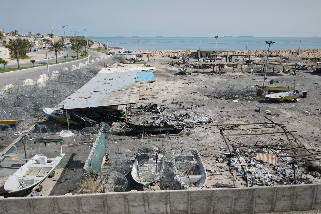 Backdropped by ships in the Strait of Hormuz, damage, according to local witnesses caused by several recent airstrikes during the U.S.-Israel military campaign, is seen on a fishing pier in the port of Qeshm island, Iran, Monday, April 13, 2026. (AP Photo/Asghar Besharati)