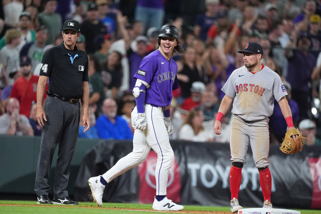 Colorado Rockies' Jake McCarthy, center, celebrates after his three-run walkoff triple as third base umpire John Tumpane, left, and Boston Red Sox third baseman Caleb Durbin, right, look on in the ninth inning of a baseball game Monday, June 22, 2026, in Denver. (AP Photo/David Zalubowski)