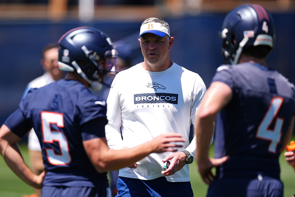 FILE - Denver Broncos offensive coordinator Joe Lombardi, center, confers with Denver Broncos quarterbacks Ian Book (5) and Blake Stenstrom (4) as they take part in drills during the NFL football team's rookie minicamp, May 10, 2025, in Centennial, Colo. (AP Photo/David Zalubowski, File)