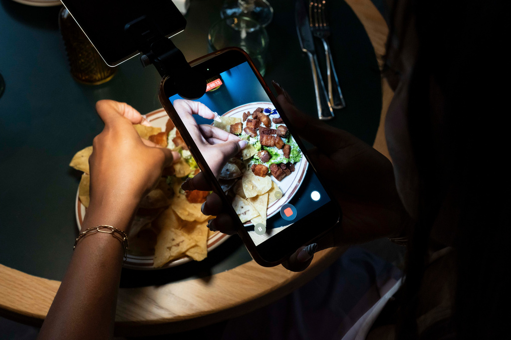 Phoenix-based content creator Aiesha Beasley films a detail shot of her chips and guacamole during the grand opening of Padeland, a venue for the racket sport padel in Chandler, Ariz., Thursday, Aug. 13, 2026. (AP Photo/Rebecca Noble)