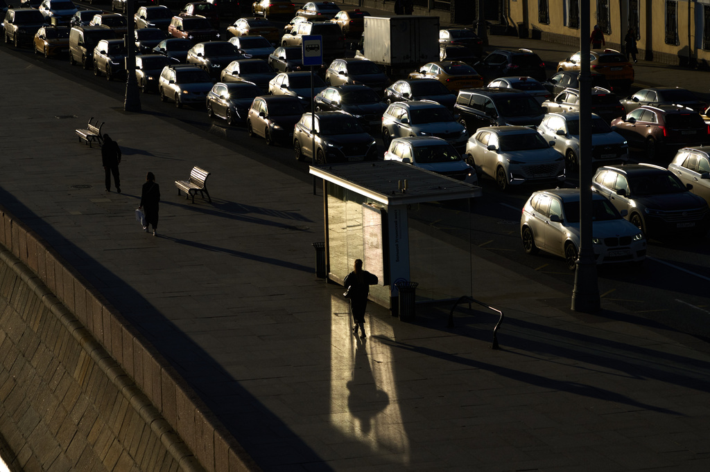 A pedestrian walks past a bus stop, in whose glass a sunbeam is reflected while cars driving along Moskvoretskaya embankment of the Moskva River near the Kremlin, during sunset in Moscow, Russia, Tuesday, April 21, 2026. (AP Photo/Alexander Zemlianichenko)