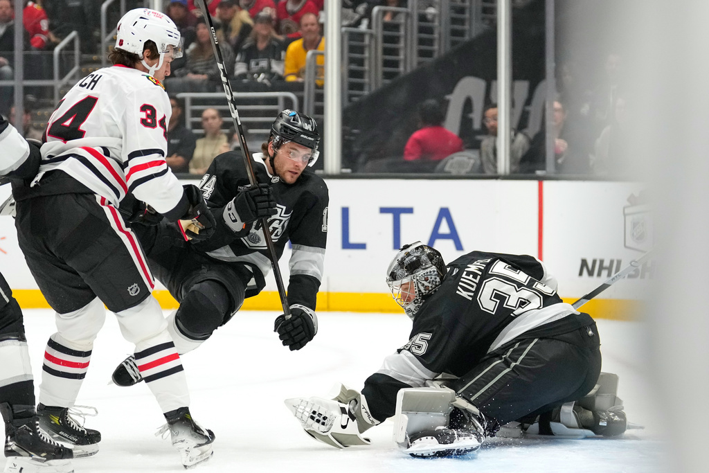 Los Angeles Kings goaltender Darcy Kuemper, right, makes a glove save as Chicago Blackhawks center Colton Dach, left, watches and right wing Alex Laferrierek trips during the first period of an NHL hockey game Thursday, Dec. 4, 2025, in Los Angeles. (AP Photo/Mark J. Terrill)