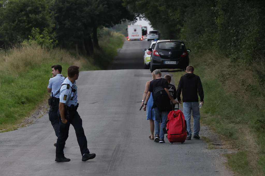 People walk past police as they leave the scene where a passenger train derailed at the village of Bjerndrup between Kliplev and Tinglev in Southern Jutland, Denmark, Friday Aug. 15, 2025. (Robert Wengler/Ritzau Scanpix via AP)