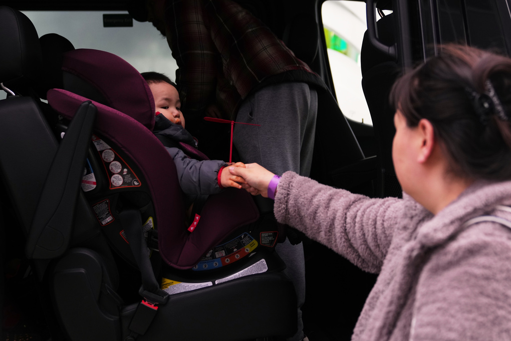 Tuck Fox holds the hand of his mother Teena as they load into a van and move to a hotel, after taking shelter at the Alaska Airlines Center in Anchorage, Alaska, due to being displaced by Typhoon Halong earlier in the month from their village of Kipnuk. (AP Photo/Lindsey Wasson)