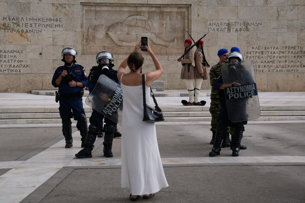 A woman takes a snapshot at the Greek parliament as Greek police stand guard near a protest during a nationwide 24-hour strike in Athens, Greece, Wednesday, Oct. 1, 2025. (AP Photo/Petros Giannakouris)