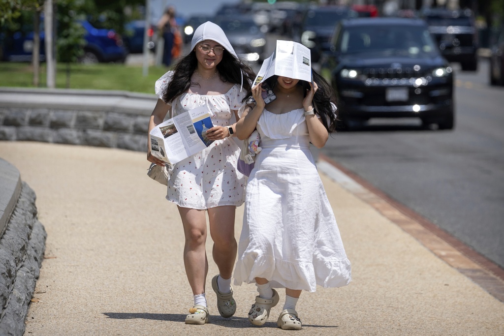 FILE - Visitors use brochures to shield themselves from the sun as they walk near the U.S. Capitol on an unseasonably hot day, June 24, 2025, in Washington. (AP Photo/Mark Schiefelbein, File)