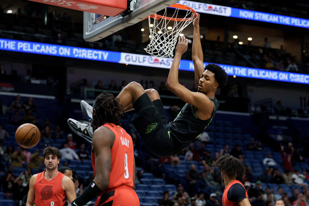 New Orleans Pelicans forward Trey Murphy III (25) hangs on the rim next Portland Trail Blazers forward Jerami Grant (9) during the first half of an NBA basketball game in New Orleans, Thursday, Dec. 11, 2025. (AP Photo/Matthew Hinton)