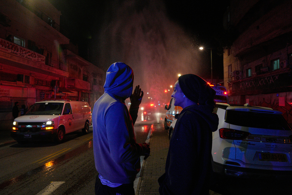 Residents look on as first responders work at the site of a missile strike in Tel Aviv, Israel, early Saturday, March 28, 2026. (AP Photo/Maya Levin)