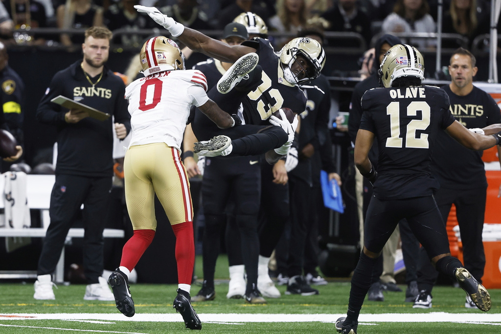 New Orleans Saints tight end Juwan Johnson, middle, is tackled by San Francisco 49ers cornerback Renardo Green (0) during the first half of an NFL football game in New Orleans, Sunday, Sept. 14, 2025. (AP Photo/Butch Dill)