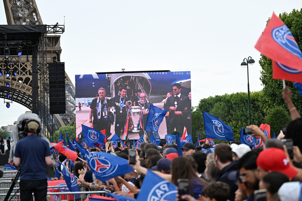 Fans cheer as a giant monitor shows PSG's head coach Luis Enrique and team upon landing, during celebrations the day after winning the Champions League title, at the Eiffel Tower, in Paris, Sunday, May 31, 2026. (AP Photo/Emma Da Silva)