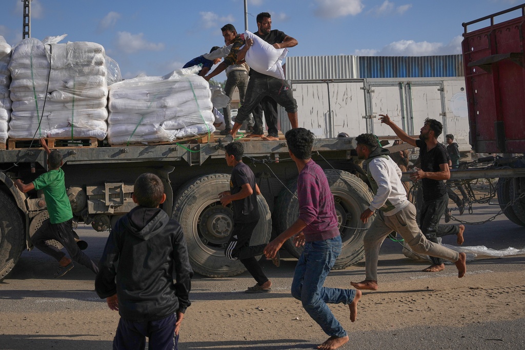 Palestinians grab sacks of flour from a moving truck carrying World Food Programme (WFP) aid as it drives through Deir al-Balah in central Gaza, Saturday, Nov. 15, 2025. (AP Photo/Abdel Kareem Hana)