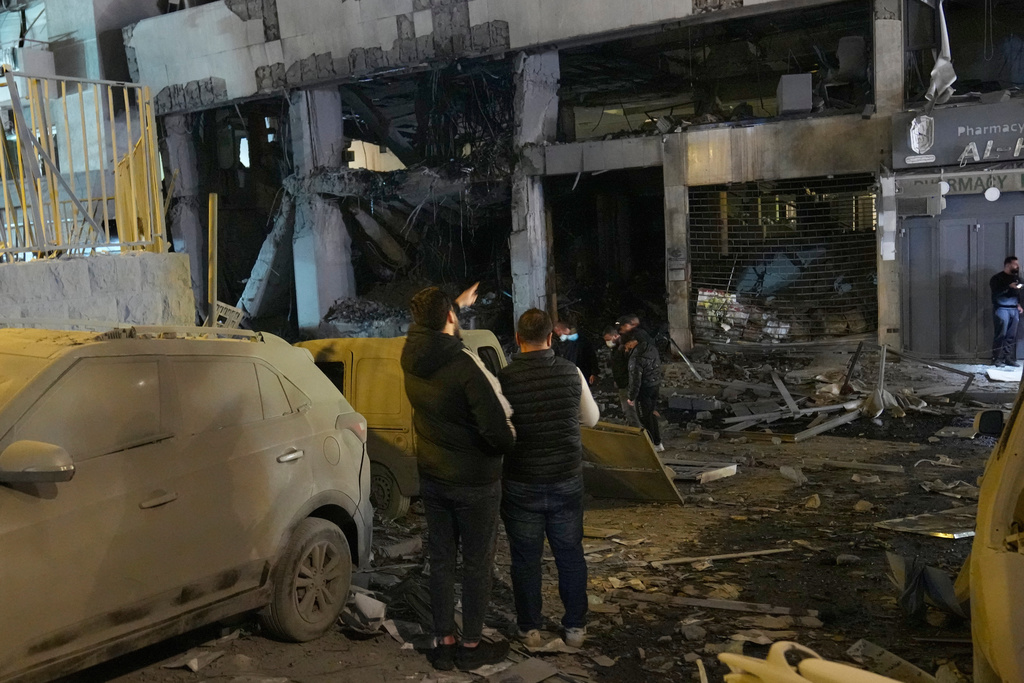 FILE - People view the destroyed branch of Al-Qard Al-Hassan, background, a non-bank financial institution run by Hezbollah, which was hit by an Israeli airstrike in central Beirut, Thursday, March 12, 2026. (AP Photo/Hussein Malla, File)