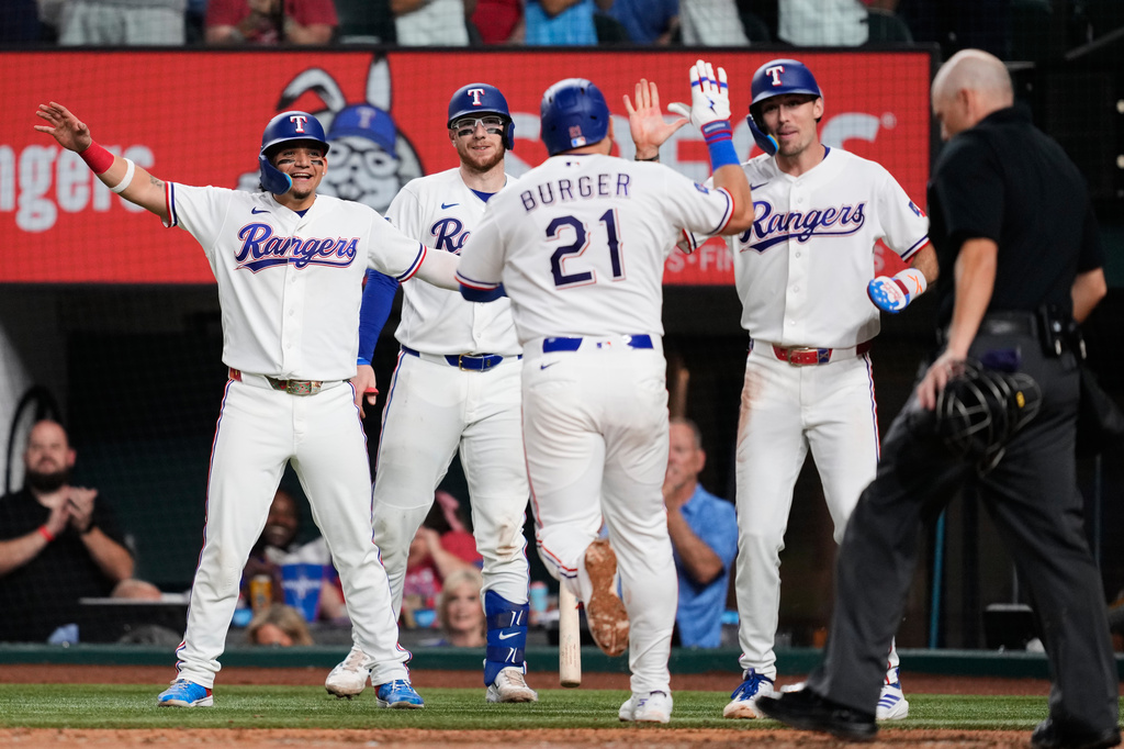 Texas Rangers' Alejandro Osuna, from left, Danny Jansen, Jake Burger (21) and Evan Carter, second from right, celebrate Burger's three-run home run as umpire Jansen Visconti, right, stands by the plate in the fifth inning of a baseball game against the Arizona Diamondbacks Wednesday, May 13, 2026, in Arlington, Texas. (AP Photo/Tony Gutierrez)