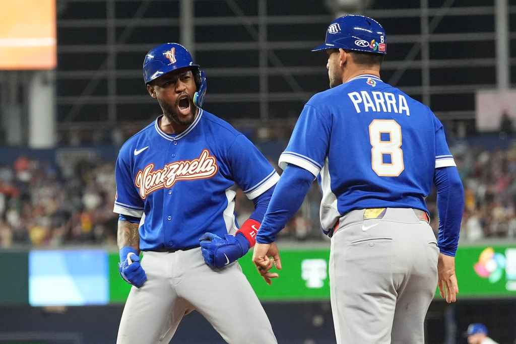 Venezuela Maikel Garcia reacts to first base coach Gerardo Parra (8) after getting on the base during the seventh inning of a World Baseball Classic semifinal game against Italy, Monday, March 16, 2026, in Miami. (AP Photo/Rebecca Blackwell)