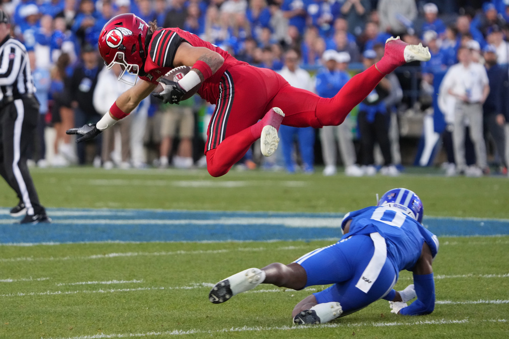 Utah wide receiver Ryan Davis, left, hurdles over BYU cornerback Evan Johnson (0) during the first half of an NCAA college football game Saturday, Oct. 18, 2025, in Provo, Utah. (AP Photo/George Frey)