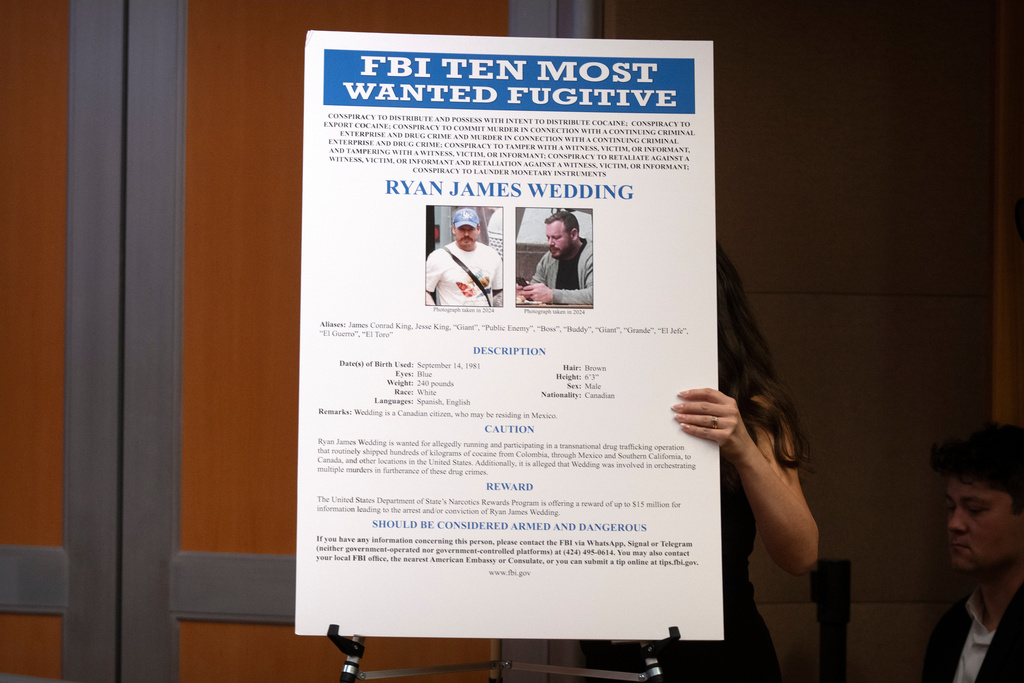 A staff member moves a wanted poster for Canadian fugitive Ryan James Wedding during a news conference at the Department of Justice, Wednesday, Nov. 19, 2025, in Washington. (AP Photo/Mark Schiefelbein)