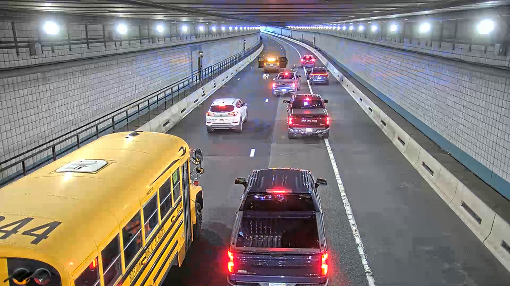 This image from surveillance video shows a Massachusetts state trooper kneeling on the highway and trying to coax a dog to get into his cruiser after the animal run through the Ted Williams Tunnel in Boston during rush hour on Thursday, Nov. 6, 2025. (Massachusetts Department of Transportation via AP)