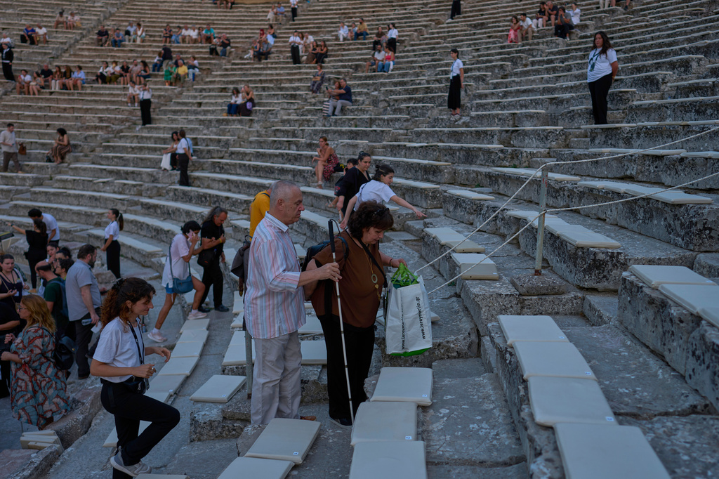 A visually impaired theatergoer and his companion make their way to their seats before a performance of Euripides' tragedy The Trojan Women, staged by the National Theatre of Greece at the Ancient Theater of Epidaurus on Sunday, Aug. 2, 2026. (AP Photo/Petros Giannakouris)