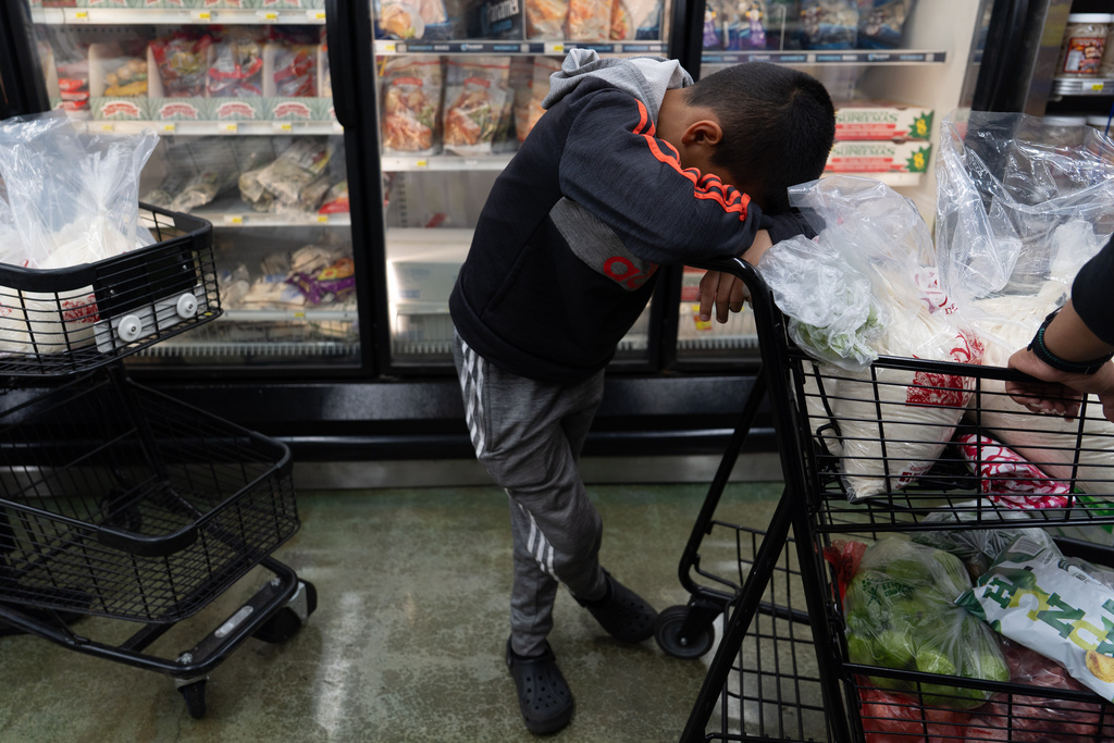 Antonio Alvarez, 11, rests his head on a shopping cart as he and his mother wait in line to buy masa, a dough used to make tamales, at Amapola Market in Downey, Calif., early Tuesday morning, Dec. 23, 2025. (AP Photo/Jae C. Hong)