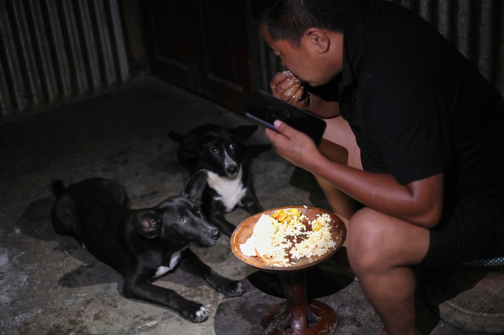 Tovi Murru, 32, eats dinner watched by his dogs inside their kitchen in Kohima, capital of the northeastern Indian state of Nagaland, Monday, July 6, 2026. (AP Photo/Yirmiyan Arthur)