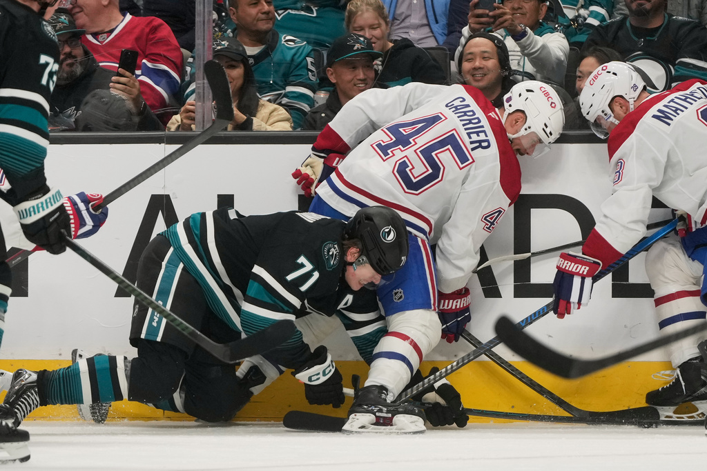 San Jose Sharks center Macklin Celebrini (71) reaches for the puck under Montréal Canadiens defenseman Alexandre Carrier (45) and defenseman Mike Matheson during the first period of an NHL hockey game in San Jose, Calif., Tuesday, March 3, 2026. (AP Photo/Jeff Chiu)