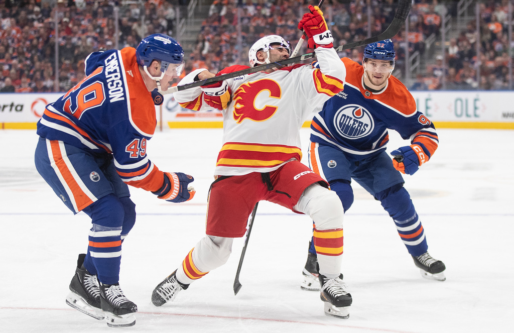 Calgary Flames' Nazem Kadri (91) gets a high stick from Edmonton Oilers' Ty Emberson (49) as Vasily Podkolzin (92) chases during first period NHL action, in Edmonton on Wednesday, Oct. 8, 2025. (Jason Franson/The Canadian Press via AP)
