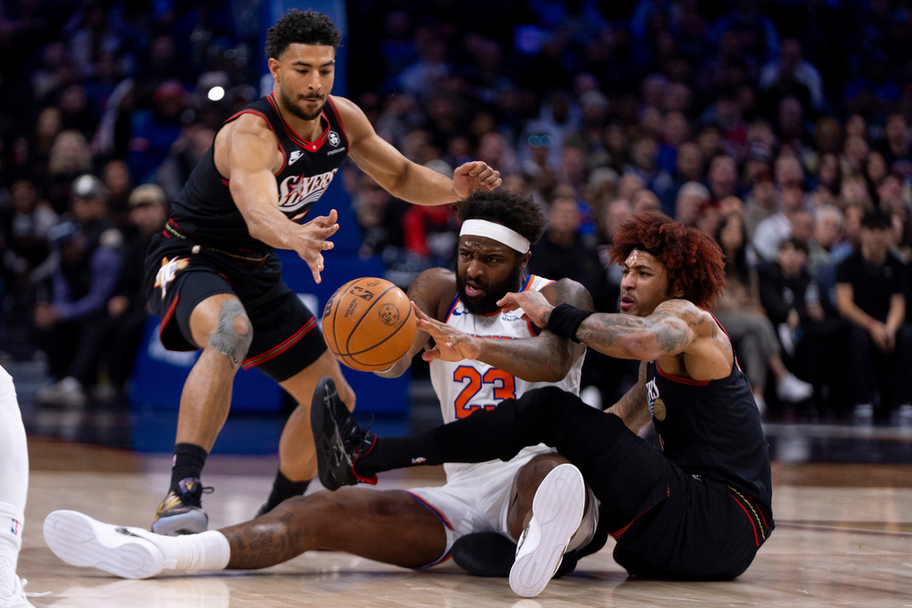 New York Knicks' Mitchell Robinson, center, tries to pass the ball with Philadelphia 76ers' Kelly Oubre Jr., right, and Quentin Grimes, left, defending during the first half of an NBA basketball game, Saturday, Jan. 24, 2026, in Philadelphia. (AP Photo/Chris Szagola)