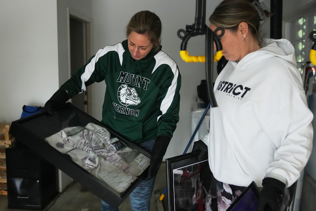Mandy McColl, right, looks over as friend Marielle Hinderman shows a jersey signed by kids coached by her husband, Todd, after it was caught in floodwaters that reached their home in the region Saturday, Dec. 13, 2025, in Burlington, Wash. (AP Photo/Lindsey Wasson)