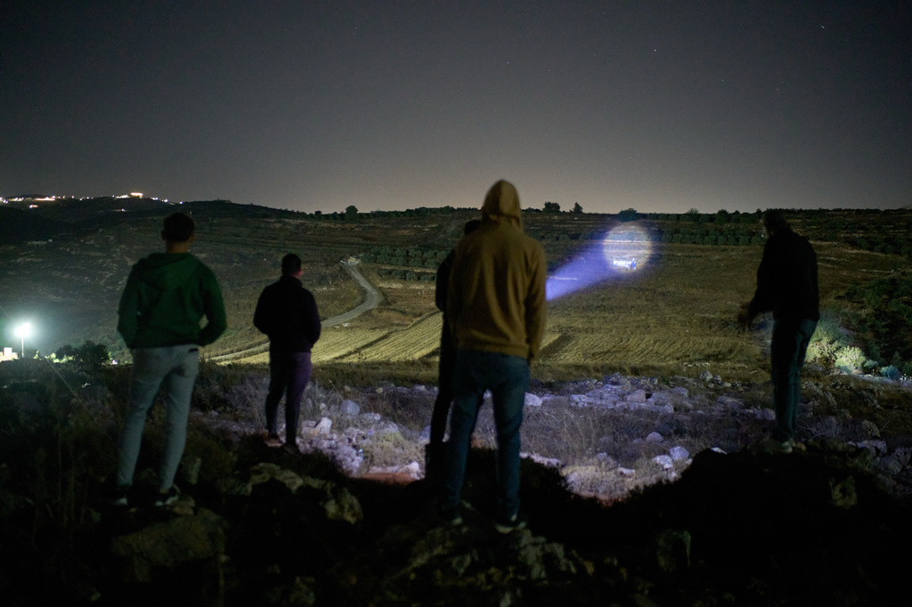 A Palestinian uses a flashlight after spotting Israeli settlers on a nearby hill while taking part in a night watch with other volunteers to guard against settler attacks on the West Bank village of Sinjil, Thursday, July 16, 2026. (AP Photo/Leo Correa)