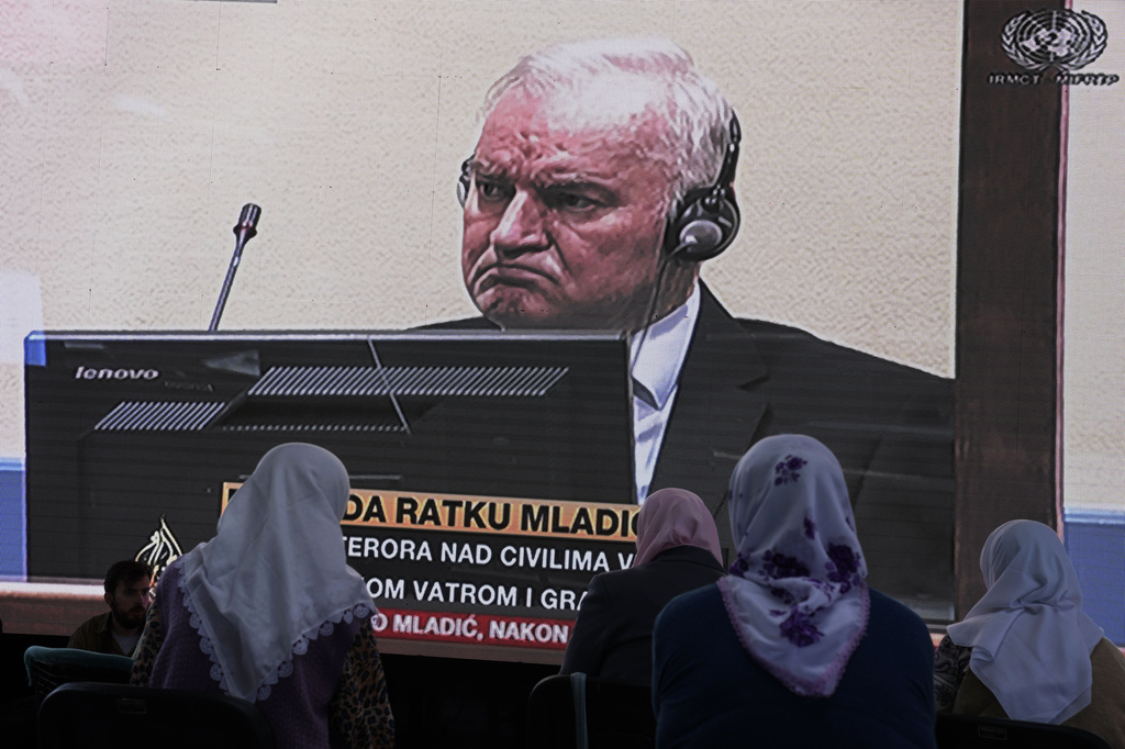 FILE - Women from Srebrenica watch a live broadcast from the Yugoslav War Crimes Tribunal in The Hague to learn the verdict for Bosnian Serb military chief Ratko Mladic, on the screen, at the memorial cemetery in Potocari near Srebrenica, eastern Bosnia, Tuesday, June 8, 2021.(AP Photo/Darko Bandic, File)