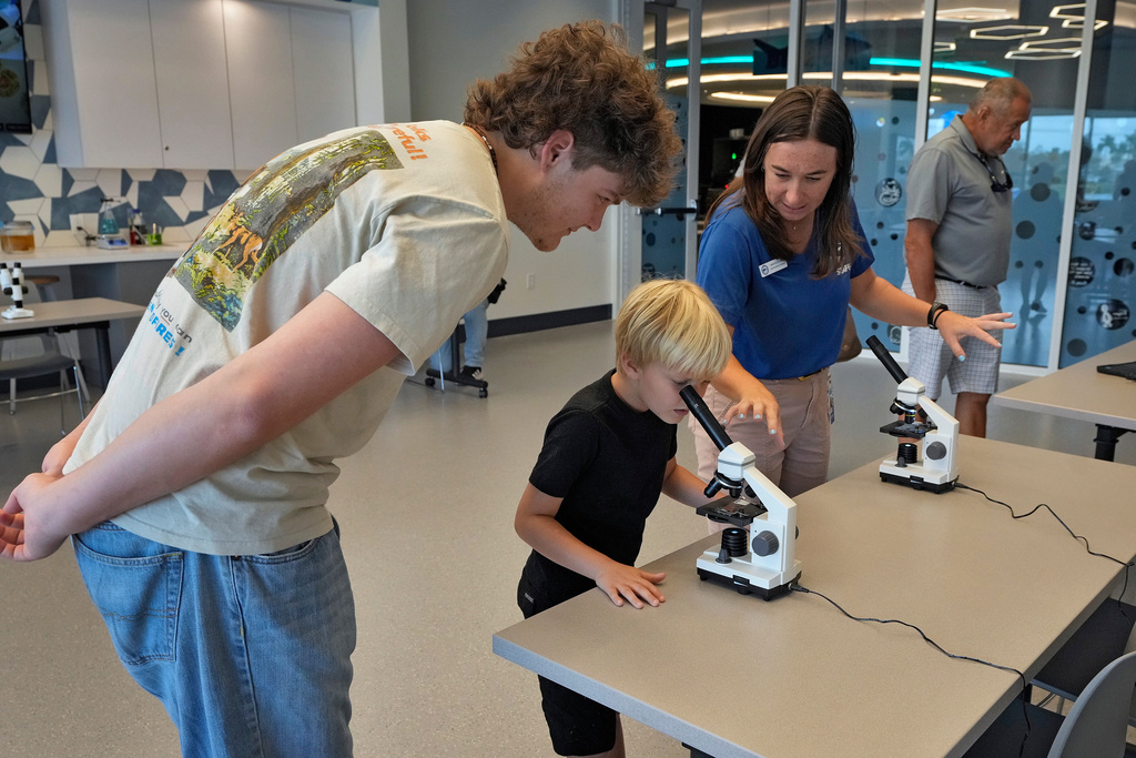 Staff member Amanda Shuman, second from right, instructs visitors using microscopes in the biomedical and immunology teaching laboratory at the Mote Science Education Aquarium, Monday, Oct. 6, 2025, in Sarasota, Fla. (AP Photo/Chris O'Meara)