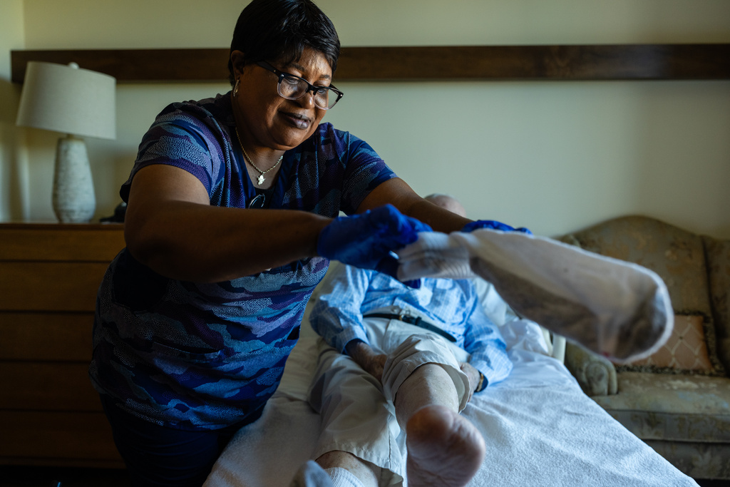 Jackie Conteh, an advanced care partner originally from Sierra Leone, helps Donald Goodness, 92, put on fresh socks in his apartment at Goodwin House Alexandria, Thursday, Oct. 16, 2025, in Alexandria, Va. (AP Photo/Eric Lee)