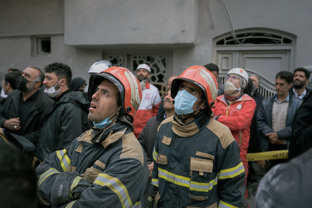 Firefighters look on as volunteers and first responders inspect the rubble and search for victims at a residential building hit in an overnight strike during the U.S.-Israeli military campaign in Tabriz, East Azerbaijan Province, northwestern Iran, Tuesday, March 24, 2026. (AP Photo/Matin Hashemi)