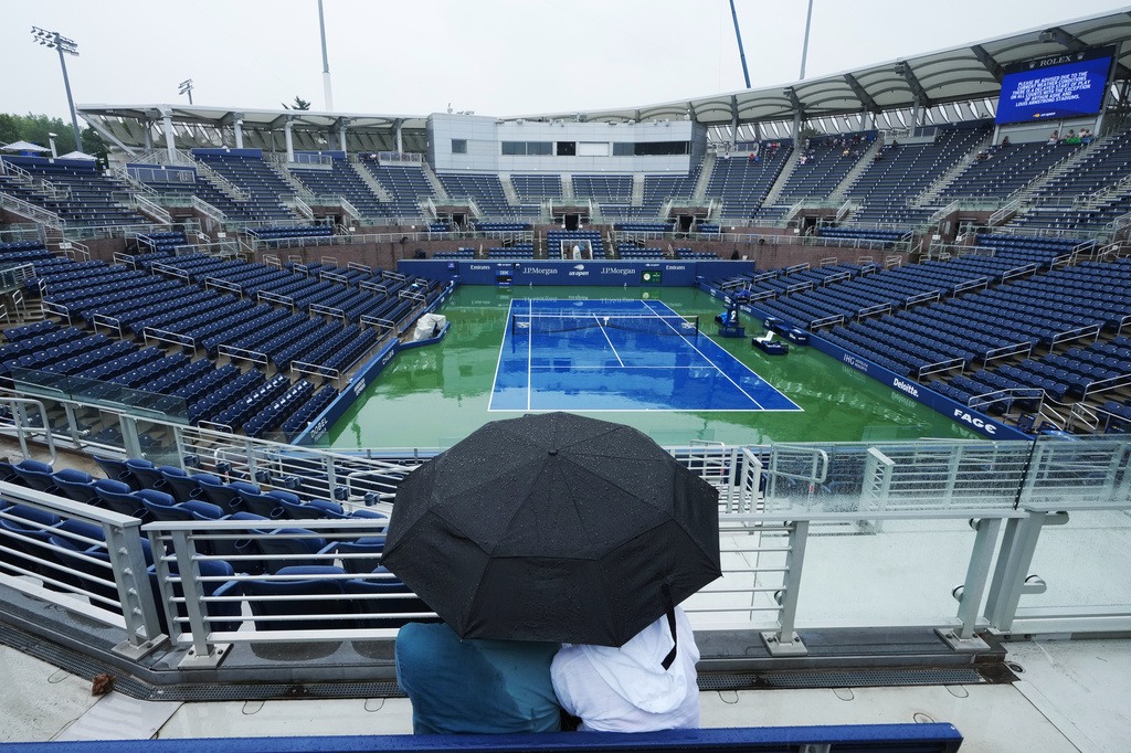 A couple sits under an umbrella during a rain delay on the Grandstand court during the first round of the U.S. Open tennis championships Tuesday, Sept. 1, 2026, in New York. (AP Photo/Kirsty Wigglesworth)