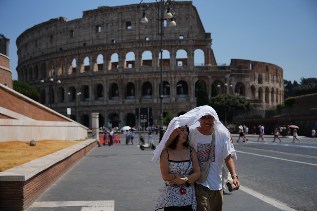 Tourists take shelter as they walk in front of the Rome'a ancient Colosseum, Saturday, Aug. 1, 2026. (AP Photo/Alessandra Tarantino)