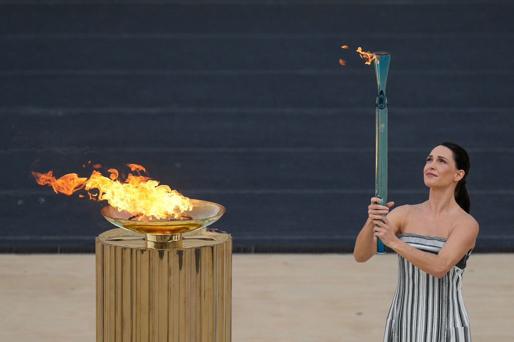 Greek actress Mary Mina, playing the role of High Priestess, lights a torch from the cauldron during the Milan Cortina 2026 Winter Olympics flame handover ceremony at Panathenaic stadium, in Athens, Greece, Thursday, Dec. 4, 2025. (AP Photo/Petros Giannakouris)