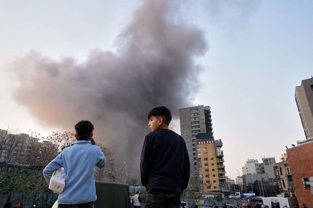 Two boys watch as smoke rises from a building nearby after an Israeli strike in central Beirut, Lebanon, Thursday, March 12, 2026. (AP Photo/Hussein Malla)