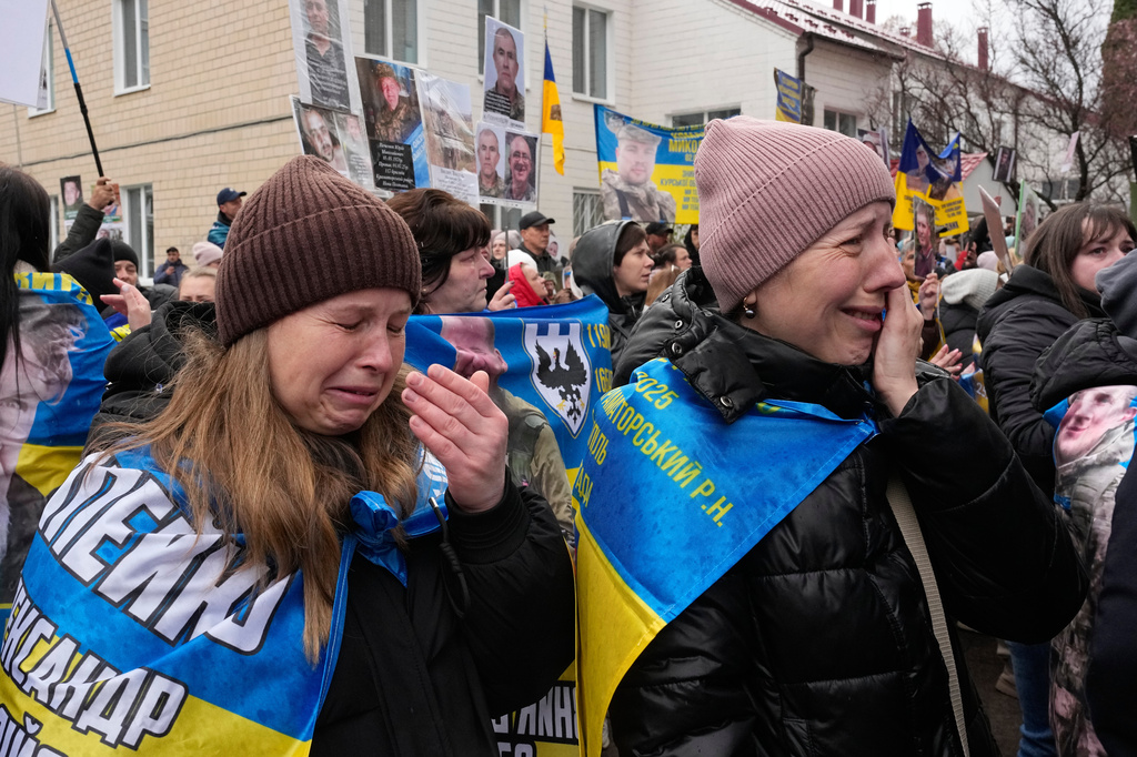 People cry as they hold hold photos of their missed relatives as Ukrainian soldiers return from captivity during a POW exchange between Russia and Ukraine in Chernyhiv region, Ukraine, Saturday, April 11, 2026. (AP Photo/Efrem Lukatsky)