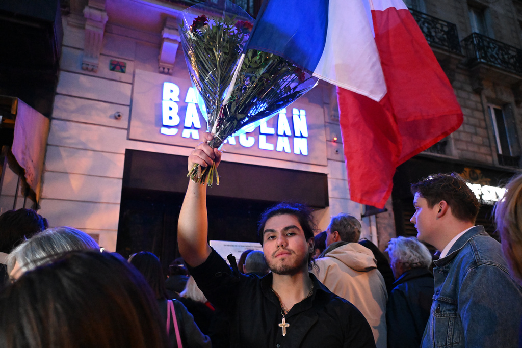 A man holds flowers and a French flag outside the Bataclan concert hall as Paris is marking the 10th anniversary of terrorist attacks that killed 132 people and injured hundreds, Thursday, Nov. 13, 2025 in Paris. (AP Photo/Emma Da Silva)