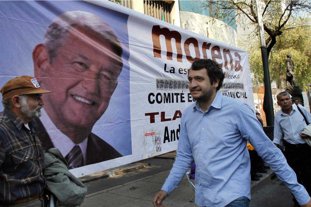 FILE - Andres Lopez Beltran, center, walks past a banner featuring an image of his father, Andres Manuel Lopez Obrador, in Mexico City, Dec. 6, 2013. (AP Photo/Marco Ugarte, File)
