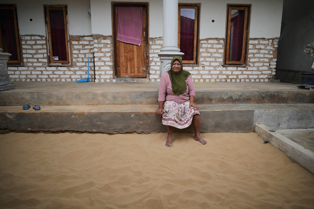 A woman sits in a sandpit outside her house in Legung Timur village in Sumenep on Madura Island, Indonesia, Tuesday, Sept. 9, 2025. (AP Photo/Dita Alangkara)