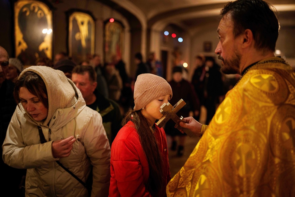 A girl kisses a cross during the service at the Holy Apostle Andrew church in Bucha, Ukraine, on Sunday, Nov. 23, 2025. (AP Photo/Evgeniy Maloletka)