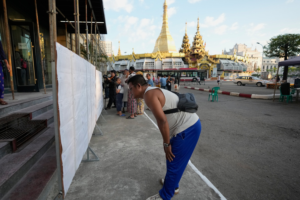 A man looks for his name on voter lists displayed outside a polling station, with Sule Pagoda in background, Sunday, Dec. 28, 2025, in Yangon, Myanmar. (AP Photo/Thein Zaw)