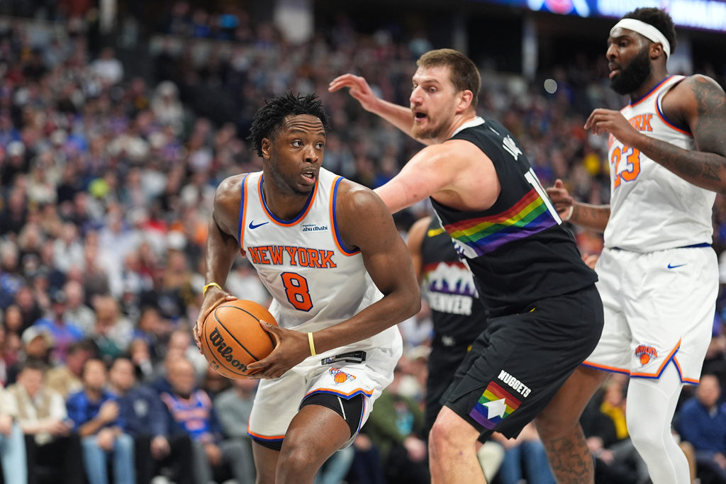 New York Knicks forward Og Anunoby, left, looks to pass the ball as New York Knicks forward Mitchell Robinson, right, blocks Denver Nuggets center Nikola Jokić in the first half of an NBA basketball game Friday, March 6, 2026, in Denver. (AP Photo/David Zalubowski)
