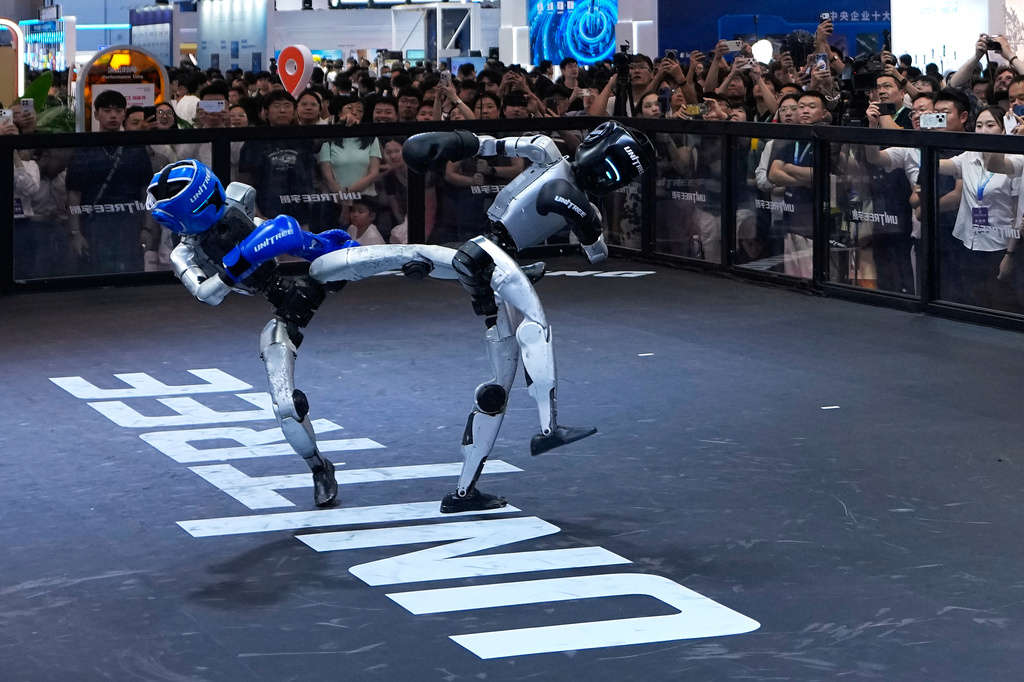 Visitors watch robots demonstrate boxing moves at a booth of Unitree, one of China's largest humanoid robot makers, during the World Robot Conference at the Beijing Yichuang International Convention and Exhibition Centre in Beijing, Wednesday, Aug. 19, 2026. (AP Photo/Andy Wong)